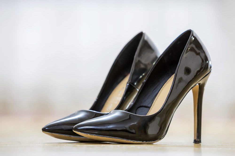Pair of fashionable high heel lacquer leather black female shoes isolated on light copy space background. Style and fashion, modern footwear concept.